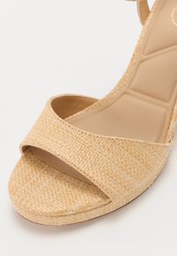 Sandale compensée beige avec texture tissée, bout ouvert et large sangle à l'avant. Doublure intérieure lisse et design de semelle robuste.