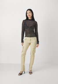 Black, long-sleeve lace top with wave pattern; beige cargo pants with side pockets and ankle zippers; black heeled sandals with straps.