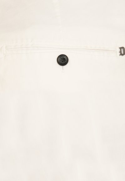 Camicia bianca con bottoni, caratterizzata da un bottone nero e una texture sottile. Include una tasca con zip e dettagli cuciti.