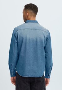 Blue denim shirt with long sleeves, button cuffs, and a collar. Features a faded texture and straight hemline. Back view shows seam details.