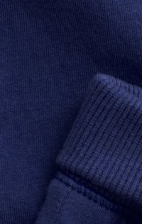 Close-up van marineblauwe gebreide stof met een gevouwen geribbelde manchet, waarbij de gedetailleerde textuur en stiksels zichtbaar zijn.