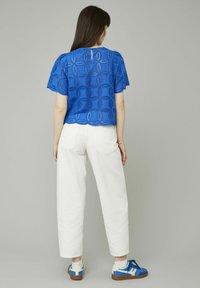 Top en dentelle bleue avec un ourlet festonné, des manches bouffantes et des découpes, associé à un pantalon large blanc et des baskets bleues.