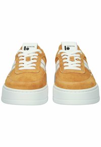 Šviesiai rudos spalvos zomšiniai sportbačiai su baltais raišteliais, baltomis juostelėmis šonuose, storu baltu padu ir „BLCKSTN“ logotipu ant liežuvėlio.