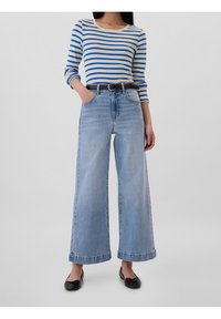 Haut à manches longues rayé bleu et blanc, jean taille haute bleu clair à large jambe, et ballerines noires. Comprend une ceinture noire.