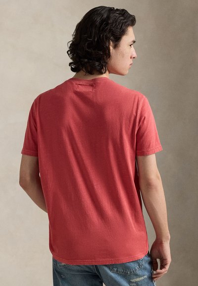 Κόκκινο κοντομάνικο μπλουζάκι από απαλό βαμβάκι, με στρογγυλή λαιμόκοψη και άνετη εφαρμογή, εμφανιζόμενο από πίσω με ελαφριά υφή.