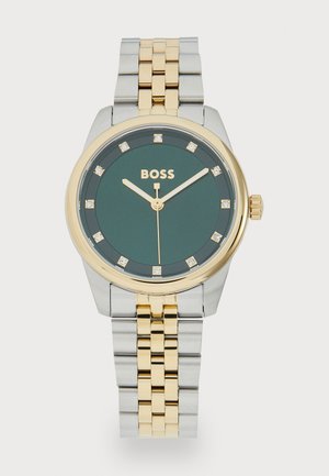 Montre en acier inoxydable doré et argenté avec un cadran vert, huit accents en diamant et des aiguilles dorées. Elle est dotée d'un bracelet en métal bicolore.