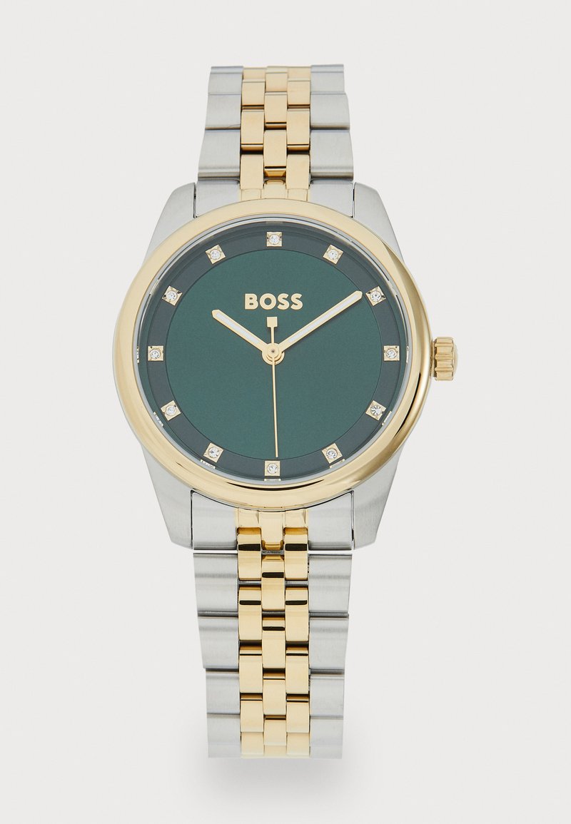 Relógio de aço inoxidável em tom de ouro e prata com mostrador verde, oito acentos de diamante e ponteiros dourados. Apresenta uma bracelete de metal bicolor.