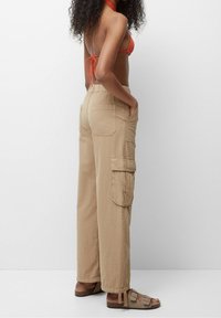 Pantalons cargo beiges à jambes larges, dotés de grandes poches latérales, d'une coupe décontractée et d'un détail de poignet aux chevilles. Tissu en coton lisse.
