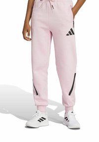 Ljusrosa joggers gjorda av mjukt tyg, med svarta ränder på sidorna och midja av elastiskt material med justerbar dragsko.