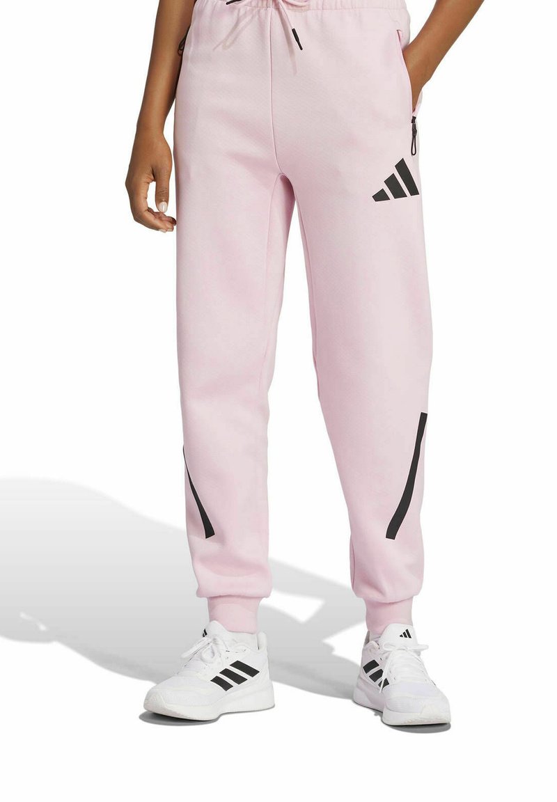 Ljusrosa joggers gjorda av mjukt tyg, med svarta ränder på sidorna och midja av elastiskt material med justerbar dragsko.