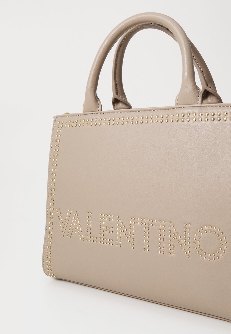 Sac à main en cuir beige avec poignées supérieures, accents en clous dorés et logo "VALENTINO" embossé à l'avant. Texture lisse et design structuré.