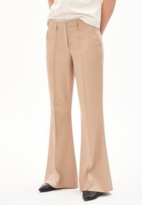 Pantalons évasés beige en tissu lisse, avec des plis sur le devant et une coupe ajustée. Accentués par une taille plate et des poches latérales.