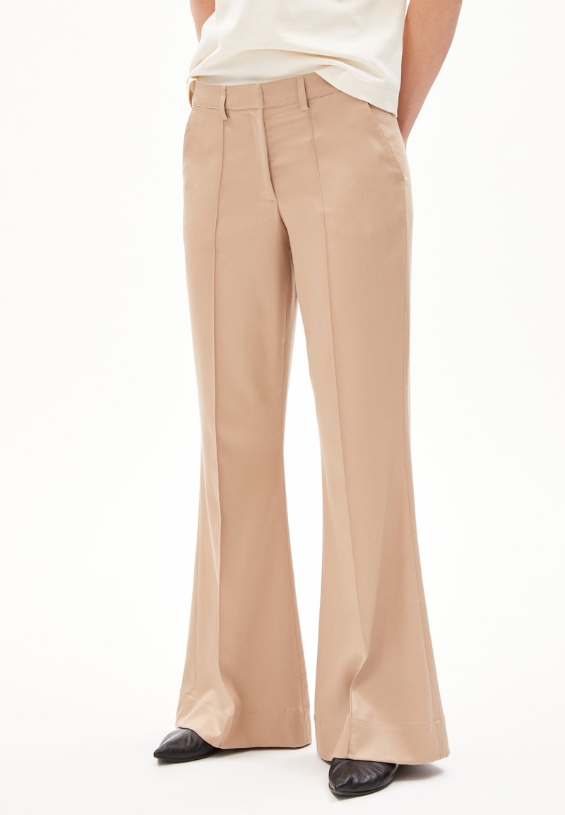 Pantalons évasés beige en tissu lisse, avec des plis sur le devant et une coupe ajustée. Accentués par une taille plate et des poches latérales.