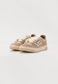 Adidași din suede de culoare maro deschis cu o talpă din cauciuc crem. Prezintă șireturi albe și un logo pe lateral într-o culoare contrastantă.