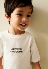 Tricou alb din bumbac cu mâneci scurte. Text imprimat în negru: „ÎNTOTDEAUNA FAIN” și „LOS ANGELES, CALIFORNIA ÎNFIINȚAT ÎN 1982.” Design simplu.