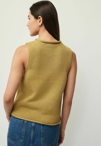 Sennepsgul ærmeløs strikket top med ribbet tekstur og rund hals, båret sammen med højtaljede blå denimjeans.