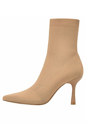 Bottine chaussette beige en maille avec bout pointu, talon stiletto fin de hauteur moyenne, design montant à la cheville et tissu texturé.