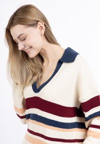 Gebreide pullover in crème met blauwe, bordeauxrode en oranje strepen. Beschikt over een v-hals en een kraag; zachte textuur en een ontspannen pasvorm.