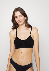 Černý bralet se nastavitelnými ramínky, měkký materiál, řasený detail uprostřed, v kombinaci s odpovídajícími kalhotkami s nízkým pasem.