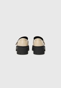 Scarpe in pelle beige con suola platform nera e apertura sul retro. Il tacco è robusto con un motivo di presa testurizzato. Presenta un dettaglio con fibbia laterale.