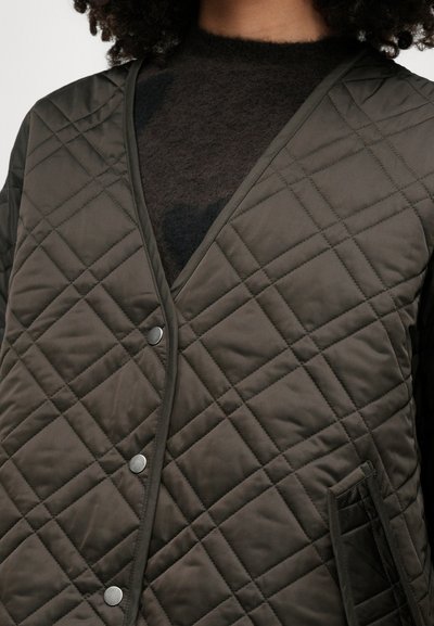 Καπιτονέ γιλέκο σε ελαιόχρωμο με σχέδιο σε σχήμα V, ασημί κουμπιά σνέπ και πλαϊνές τσέπες. Ο υφασμάτινος ιστός διαθέτει διαμαντοειδές μοτίβο.