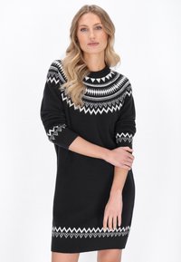 Abito nero a maglia con un motivo geometrico bianco sul colletto e sui polsini, maniche lunghe e una silhouette aderente che termina sopra il ginocchio.