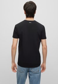 Black crewneck t-shirt made of cotton, featuring short sleeves and a small white logo "HUGO" on the back near the neckline.
