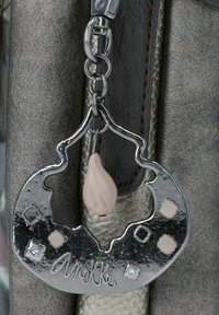 Portachiavi in metallo argentato con un pendente decorativo, presenta una finitura in cromo lucido, un accento rosa chiaro e il nome del marchio inciso, "Anekke."