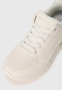 Sneaker bianco in pelle perforata, con punta rotonda e lacci piatti. Caratterizzata da una soletta imbottita e un marchio discreto sulla linguetta.