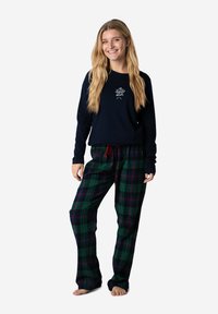 Marineblauwe lange mouwen shirt met witte borduursels, gecombineerd met groene geruite broek met rode trekkoorden. Katoenen stof, ontspannen pasvorm, volledige lengte.