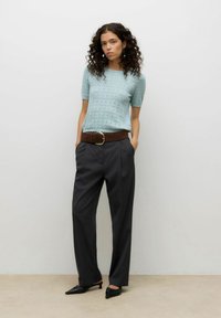 Jasnoniebieska bluzka z krótkim rękawem o teksturowanym wzorze, w połączeniu z ciemnoszarymi spodniami o szerokich nogawkach i brązowym paskiem z dużą klamrą. Czarne buty.