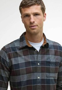 Flanellen overhemd in donkergrijs, zwart en bordeaux geruit patroon. Heeft een button-down kraag en een borstzak. Merkenlabel zichtbaar op de zak.