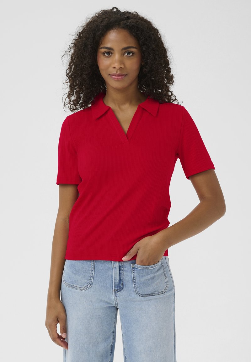 Polo rouge à rayures avec un col en V et des manches courtes. Modèle le portant avec un jean en denim bleu clair. Texture lisse, design ajusté.
