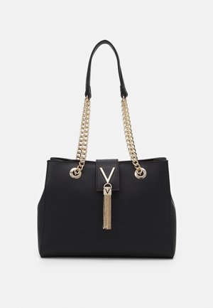 Bolso negro con asas de cadena dorada, cierre frontal con detalle metálico en forma de V y borla dorada colgante.