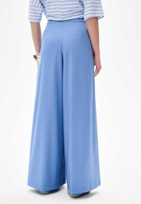 Lichtblauwe wijde broek van gladde stof, met een hoge taille en taaie naden, van achteren getoond.