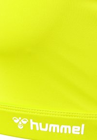 Neon żółty materiał sportowy o gładkiej fakturze z białym logo "hummel" wzdłuż dolnej krawędzi, z dodatkowym graficznym detalem pszczoły.