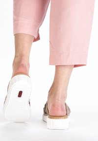 Sandal with a beige upper and white, textured rubber sole. Features adjustable straps and a cushioned footbed for comfort.