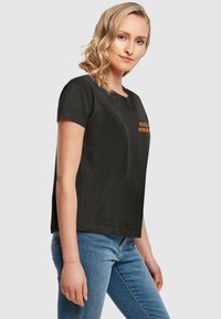 Sort bomulds-t-shirt med korte ærmer, prydet med orange tekst på forsiden. Designet er afslappet med en løs pasform og rund halsudskæring.