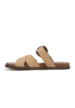 Beige suède sandaal met gekruiste bandjes en een decoratief accent bij de hiel. Platte bruine zool en een gestructureerd voetbed voor comfort.