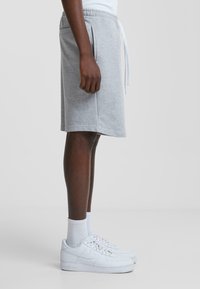 Shorts en coton gris avec une taille élastique et un cordon blanc, dotés de poches latérales et d'une coupe décontractée, portés avec des baskets blanches.