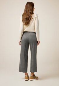 Graue Wide-Leg-Hosen mit glatter Textur, elastischem Bund und umgeschlagenen Säumen, kombiniert mit braunen und goldenen Sneakers.