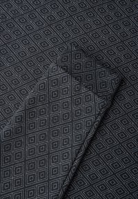 Sort stof med et geometrisk diamantmønster i hvidt. Glat tekstur, foldet i et hjørne. Designet til forskellige tekstilapplikationer.
