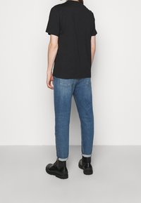 Černé bavlněné tričko s krátkým rukávem v kombinaci s modrými rovnými džíny, opatřenými manžetami, a černými kotníkovými botami. Jednoduchý a pohodlný outfit.