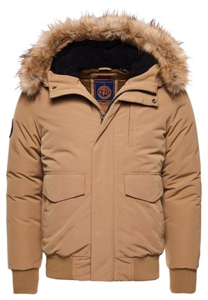 Giacca a vento marrone con cappuccio in pelliccia sintetica, zip frontale, due grandi tasche con patta, polsini e orlo a coste, e un morbido rivestimento interno.