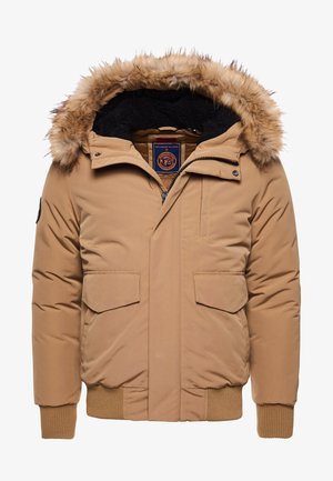 Chaqueta inflable marrón con capucha de pelaje sintético, cremallera frontal, dos grandes bolsillos con solapa, puños y dobladillo acanalados, y un suave forro interior.