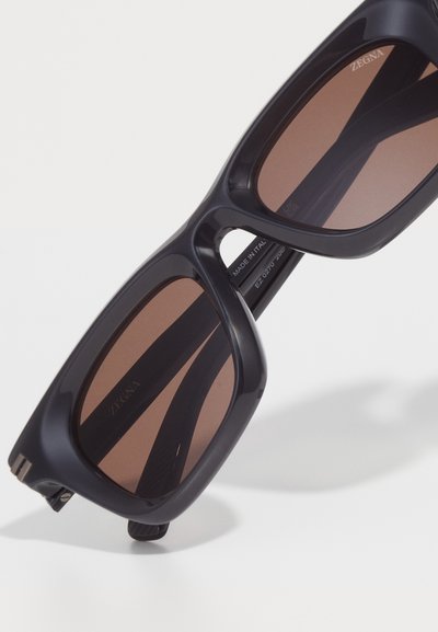 ZEGNA sunglasses with a black plastic frame and brown tinted lenses. Features a partially open design and silver hardware accents.