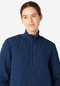Námořnická prošívaná bunda s vysokým límcem, předním zipem a vzorem v diamantech. Obsahuje texturovanou tkaninu a dvě boční kapsy.
