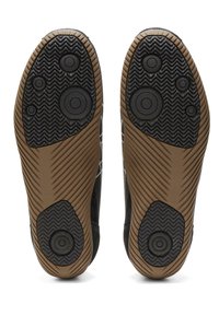 Černé sportovní boty s podrážkami obsahujícími texturovaný gumový grip s kruhovými akcenty a hnědým bočním panelem. Navrženo pro trakci a odolnost.