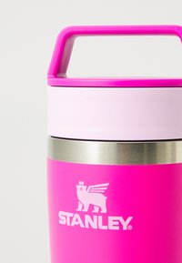 Lysende rosa Stanley isolert flaske med rosa håndtak og rustfritt stålband nær toppen.