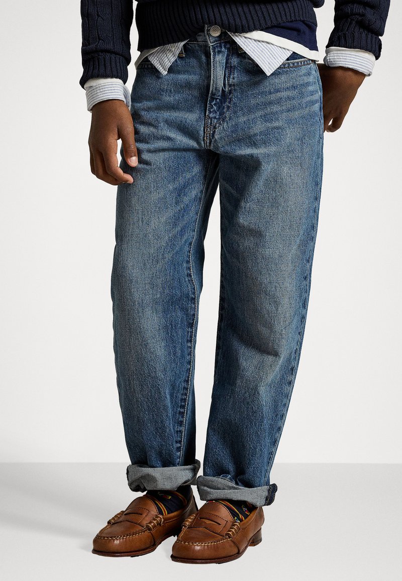 Modré džínsy s uvoľneným strihom, s vyblednutým praním, designom s piatimi vreckami a ruličkovými manžetami. V páre s hnedými mokasínami.